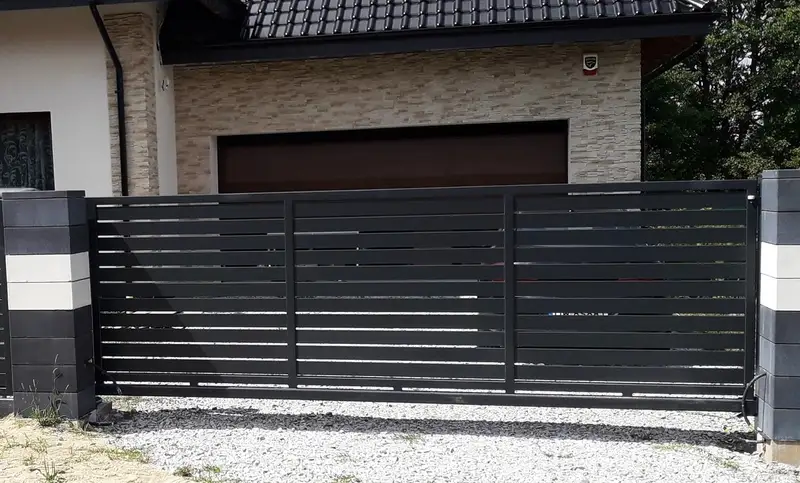 Antracytowa brama przesuwna i ogrodzenie z profili przed domem z garażem